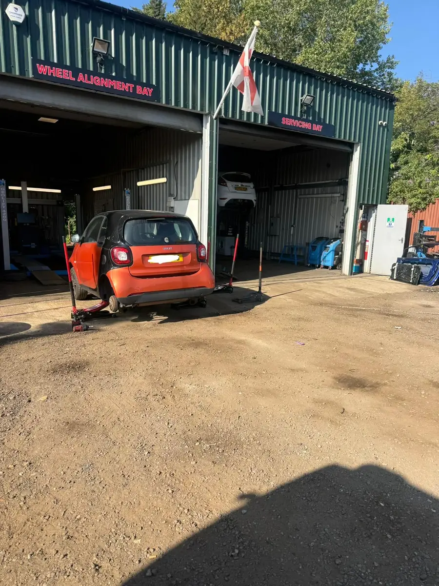Front of the Chertsey Tyres & Service Centre workshop units with a small car on a jack outside the bays