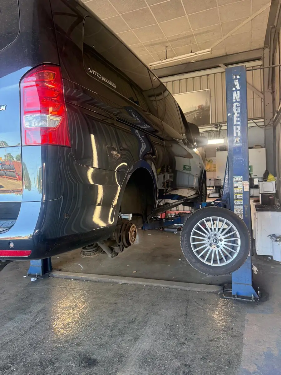 A people carrier on a two-post lift with a wheel removed inside the workshop