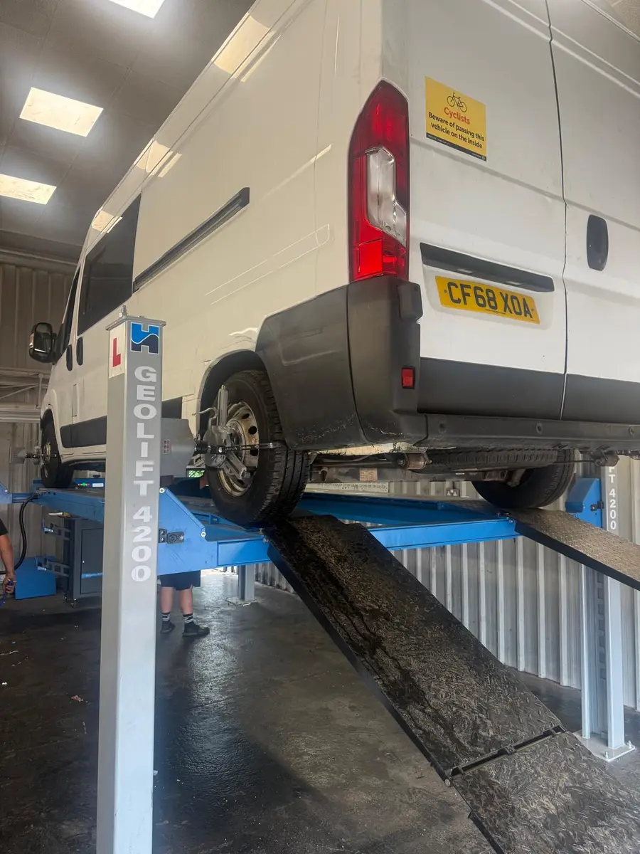 A white van on the wheel alignment ramp with alignment equipment beside it