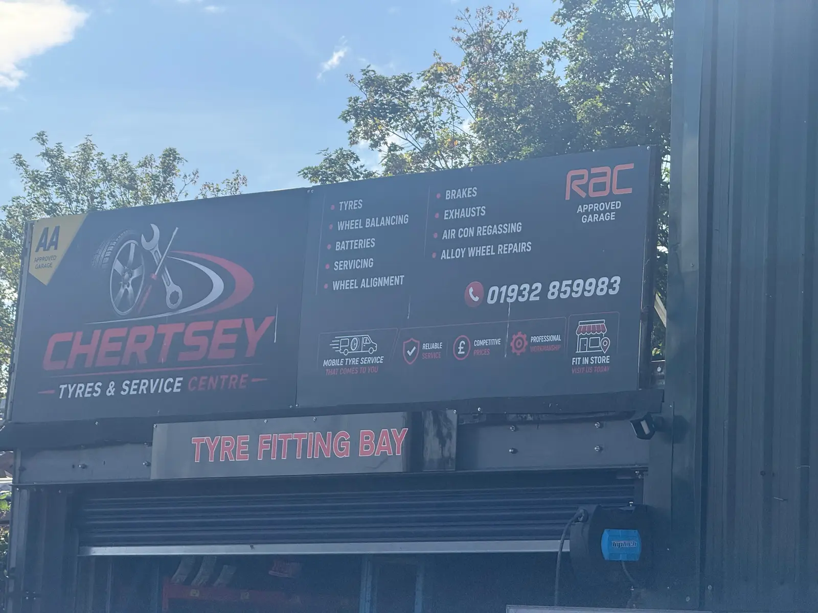 Chertsey Tyres & Service Centre sign above the tyre fitting bay listing tyres, wheel balancing, batteries, servicing, wheel alignment, brakes, exhausts, air con regassing and alloy wheel repairs, with the phone number 01932 859983